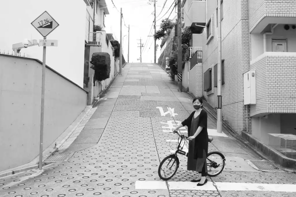  A woman pointing towards 'that hill,' the steepest slope on the school route, which has a 17% inclinein Chikusa-ku Nagoya. She is indicating that this hill is the biggest obstacle on the route.