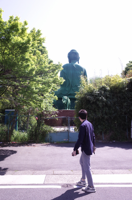 A man walking, surprised by the unexpected presence of Nagoya's green Buddha in Toganji temple in Nagoya.