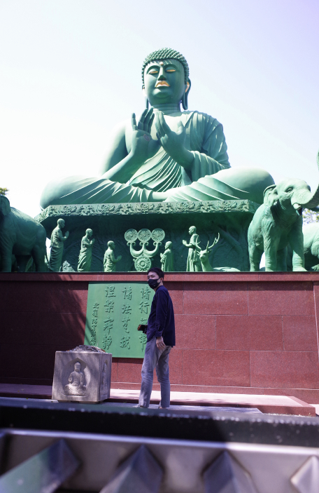 A man standing in front of Nagoya's Green Buddha in Toganji, Nagoya.