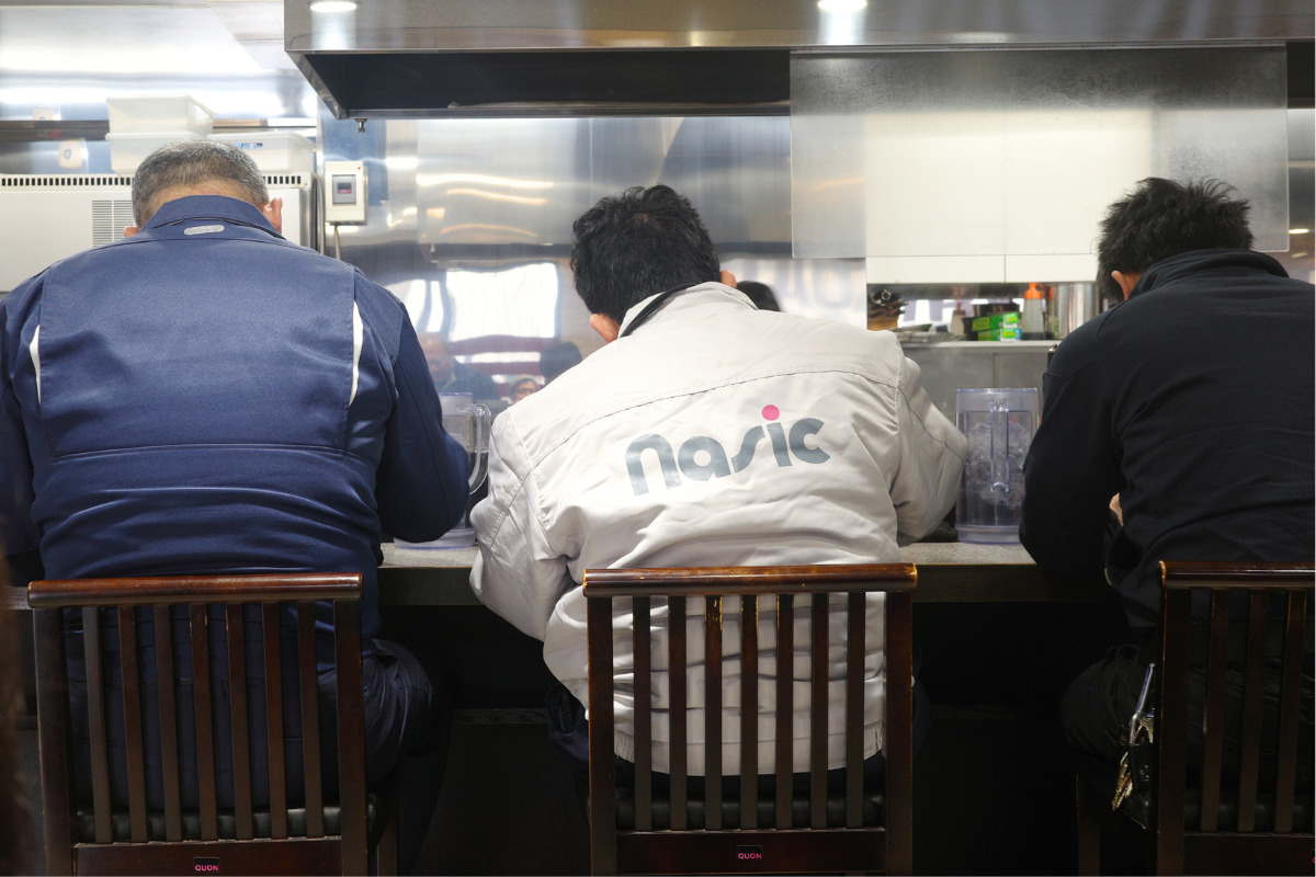 Men enjoying a bowl of delicious ramen at the counter of Hachiryu in Nagoya.