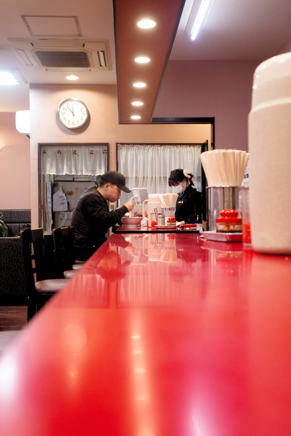 Man savoring a bowl of ramen in Nagoya, seated at a red long counter table at Chika Ichiban.