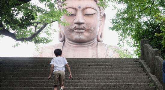 A child climbing the steps towards The Great Buddha of Shurakuen, creating a sense of awe and scale.