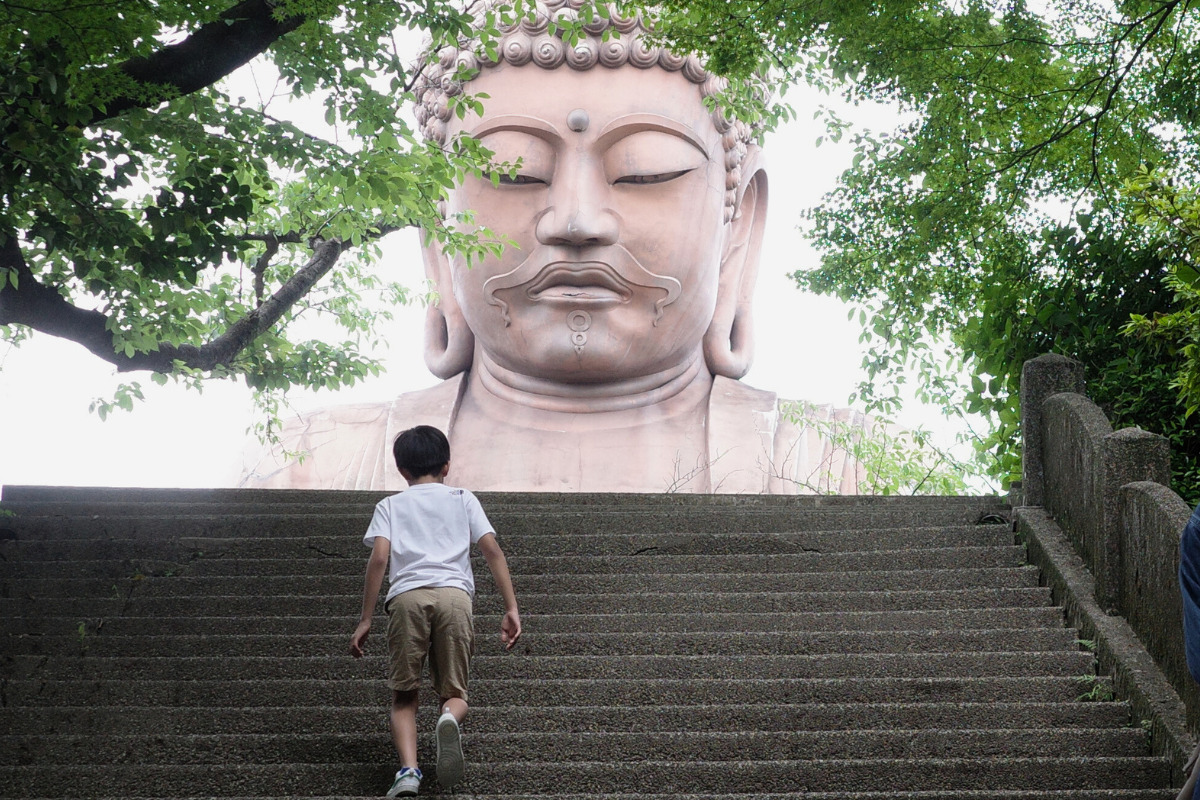 A child climbing the steps towards The Great Buddha of Shurakuen, creating a sense of awe and scale.