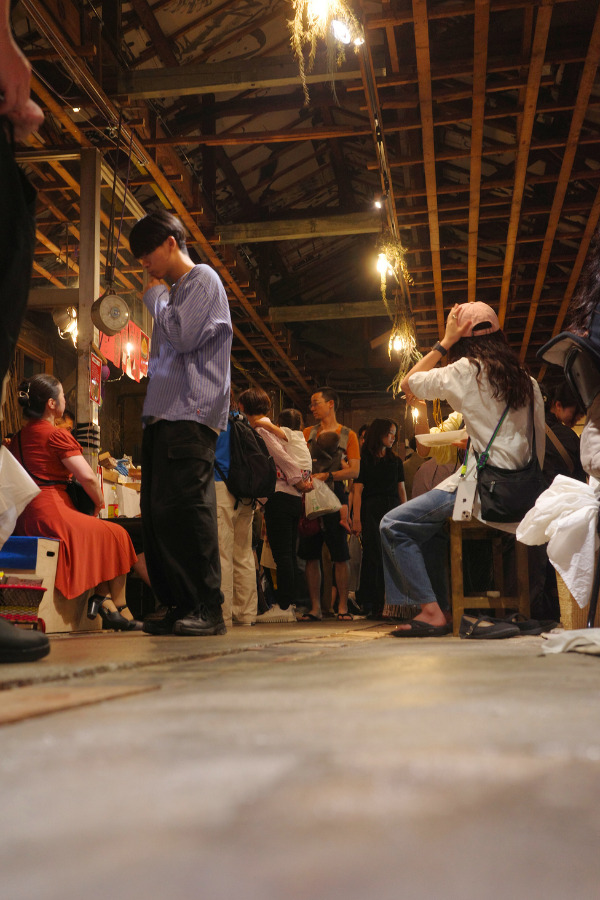 A lively scene inside Kinjo Market, with people mingling and enjoying the atmosphere under the wooden beams of the market's ceiling